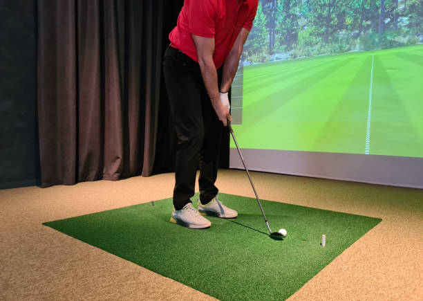 Golf player playing golf indoors on golf simulator closeup. Driving range with screen for golf and golfer legs