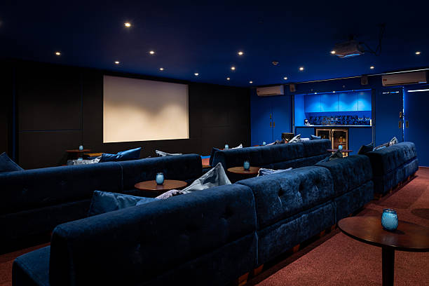 Wide-view of a private cinema room with a large display screen and rows of sofa seats with built-in ceiling lights and carpet flooring in Newcastle, England.